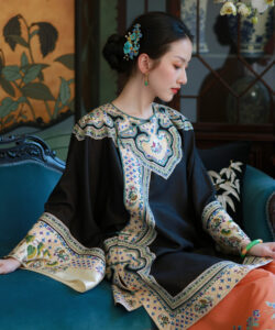 Photograph of a delicate asian woman in traditional embroidered black and gold robe seated on teal sofa with floral decor
