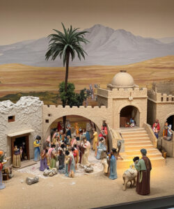 Photograph-of-a-detailed-diorama-depicting-biblical-nativity-scene-with-diverse-figures-desert-backdrop-and-ancient-architectural-structures