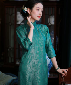 Photograph of a fair skinned asian woman in a teal silk cheongsam adorned with floral hairpiece standing in a traditional room