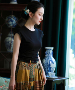 Photograph of a fair skinned asian woman in black top floral skirt holding purse in a traditional room with blue vases