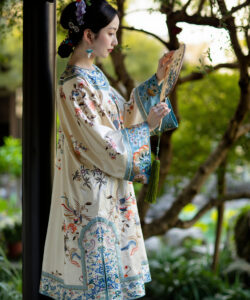 Photograph of a fair skinned asian woman in ornate traditional chinese attire holding a fan standing in a lush garden