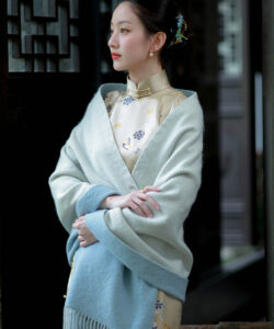 Photograph of a fair skinned asian woman in traditional chinese attire with blue and gold floral embroidery draped in a shawl