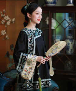 Photograph of a fair skinned asian woman in traditional black chinese dress holding intricately decorated fans in an ornate room
