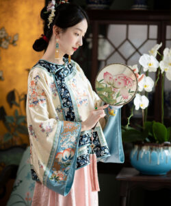 Photograph of a fair skinned dark haired woman in traditional chinese attire holding a floral fan surrounded by ornate decor