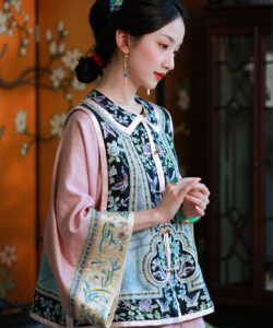 Photograph of a fair skinned red lipped asian woman in traditional chinese attire standing against an ornate floral patterned background