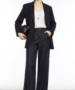 Photograph of a fair skinned woman in a black blazer white top high waisted black pants sunglasses holding a black clutch