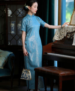 Photograph of a fair skinned woman in a blue silk cheongsam playing a vintage piano surrounded by antique decor