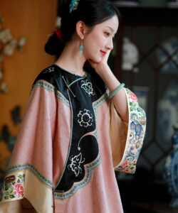 Photograph of a fair skinned woman in traditional chinese attire featuring pink and black fabric with floral embroidery in a room