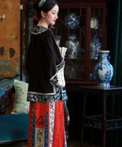 Photograph of a fair skinned woman in traditional chinese attire holding books standing in a room with antique furniture and decor