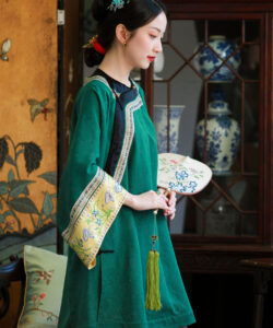 Photograph of a fair skinned woman in traditional green chinese attire holding a floral fan with ornate background decor