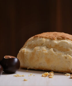Photograph-of-a-freshly-baked-loaf-of-bread-with-three-dark-shiny-cherries-and-crumb-pieces-on-a-wooden-surface