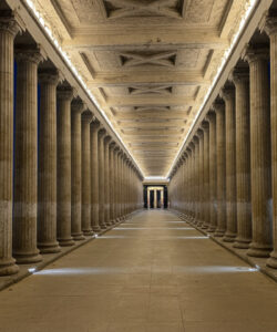 Photograph-of-a-grand-illuminated-neoclassical-colonnade-at-night-with-tall-stone-columns-symmetrical-architecture-and-distant-city-lights