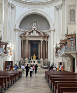 Photograph-of-a-grand-ornate-church-interior-with-marble-columns-wooden-pews-altar-with-a-gold-cross-and-a-few-visitors