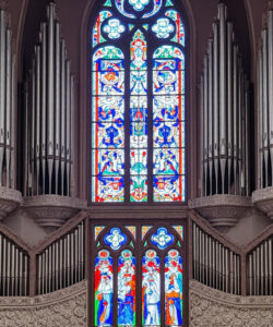 Photograph-of-a-grand-ornate-church-organ-with-colorful-stained-glass-windows-above-intricate-woodwork-and-a-majestic-pipe-organ