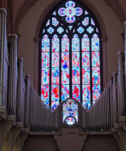 Photograph-of-a-grand-pipe-organ-with-intricate-carvings-a-large-colorful-stained-glass-window-and-Gothic-architectural-elements