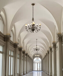 Photograph-of-a-grand-symmetrical-arched-corridor-with-large-windows-ornate-chandeliers-and-classical-architectural-details