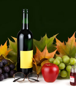 Photograph-of-a-green-wine-bottle-red-apple-grapes-glasses-and-jars-against-a-dark-green-background