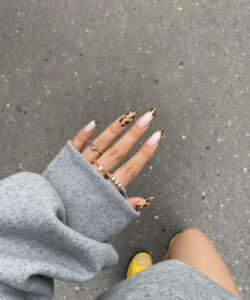 Photograph of a hand with leopard print nails wearing a grey sweater yellow shoes on a grey concrete surface