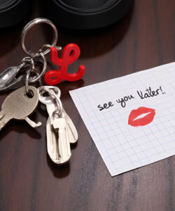 Photograph-of-a-keychain-with-keys-a-red-lipstick-shaped-key-and-a-note-saying-see-you-later-on-a-wooden-surface