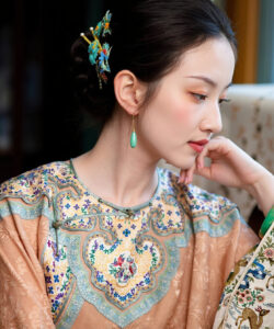 Photograph of a light skinned woman in traditional chinese attire adorned with intricate embroidery teal earrings and floral hairpiece