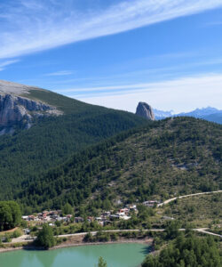 Photograph-of-a-lush-green-valley-with-a-turquoise-lake-surrounded-by-towering-mountains-under-a-clear-blue-sky