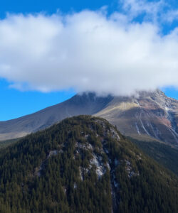 Photograph-of-a-majestic-mountain-peak-with-a-fluffy-white-cloud-surrounded-by-lush-green-forests-under-a-vivid-blue-sky