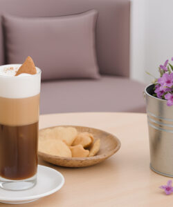 Photograph-of-a-minimalist-cafe-scene-featuring-a-frothy-coffee-topped-with-a-cookie-surrounded-by-flowers-and-pastries