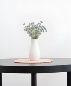 Photograph-of-a-minimalist-round-black-table-with-a-white-vase-of-blue-flowers-beige-chairs-white-background