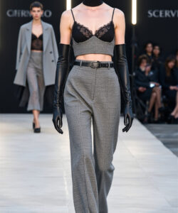 Photograph of a model with short dark hair wearing black lace bra grey high waisted pants black gloves and choker