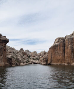 Photograph-of-a-narrow-rocky-canyon-with-a-calm-river-in-the-center-under-a-partly-cloudy-sky