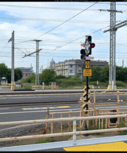 Photograph-of-a-railway-crossing-with-a-signal-overpass-and-urban-background-under-a-cloudy-sky