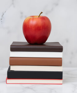 Photograph-of-a-red-apple-atop-a-stack-of-books-on-a-white-marble-surface-against-a-gray-marble-wall