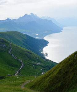 Photograph-of-a-red-clad-person-on-a-grassy-hill-overlooking-a-serene-blue-lake-and-surrounding-lush-green-mountains
