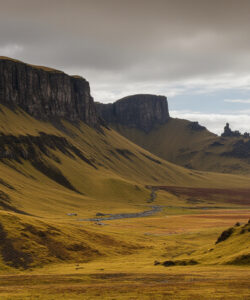 Photograph-of-a-rugged-moss-covered-mountain-landscape-under-cloudy-skies-with-a-winding-stream-and-distant-rock-formations