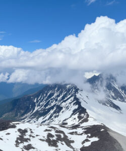 Photograph-of-a-rugged-snow-capped-mountain-peak-under-a-partly-cloudy-sky-with-lush-valleys-in-the-background