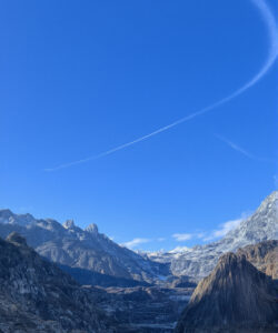 Photograph-of-a-rugged-snow-dusted-mountain-range-under-a-clear-blue-sky-with-a-wispy-white-contrail