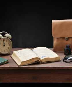 Photograph-of-a-rustic-wooden-table-with-a-vintage-alarm-clock-open-book-glasses-notebook-and-a-leather-satchel