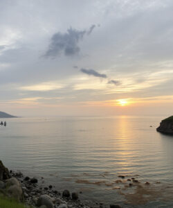 Photograph-of-a-serene-coastal-landscape-at-sunset-with-a-calm-sea-green-hills-and-a-partly-cloudy-sky