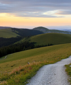 Photograph-of-a-serene-mountain-landscape-at-sunset-featuring-a-winding-gravel-path-lush-green-hills-and-distant-rocky-peaks