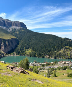 Photograph-of-a-serene-mountain-landscape-with-a-turquoise-lake-greenery-distant-snow-capped-peaks-and-a-small-village-below