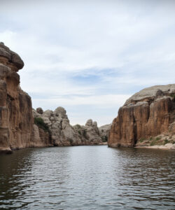 Photograph-of-a-serene-narrow-canyon-with-rugged-reddish-brown-cliffs-and-a-calm-reflective-river-in-the-foreground