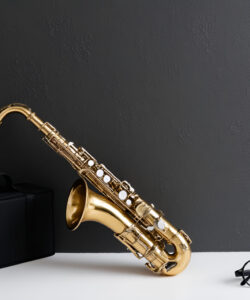 Photograph-of-a-sleek-black-briefcase-a-shiny-golden-saxophone-and-black-framed-glasses-on-a-minimalist-dark-gray-wall