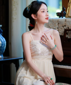 Photograph of a slender asian woman in a cream dress seated beside a piano with intricate hair accessories in a room
