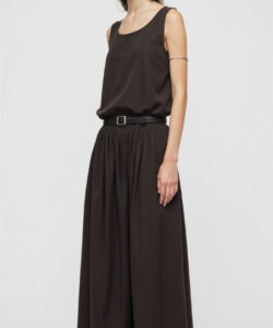 Photograph of a slender dark haired woman in a sleeveless black top and high waisted black skirt standing against a plain white background