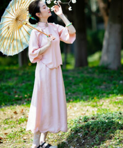 Photograph of a slender fair skinned asian woman in a pink traditional chinese outfit holding an umbrella surrounded by trees