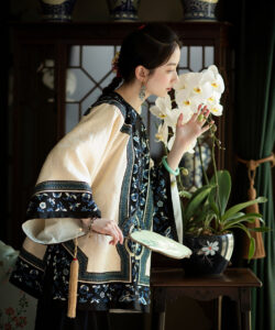Photograph of a slender fair skinned woman in traditional chinese attire admiring white orchids with detailed blue and gold embroidery