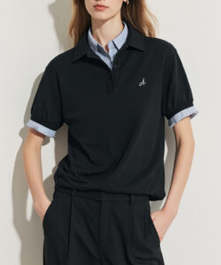 Photograph of a slender fair skinned woman with long blonde hair wearing black polo shirt glasses and high waisted black trousers