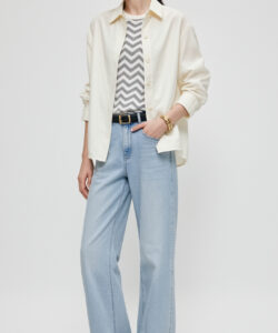Photograph of a slender light skinned woman in a white cap beige shirt gray striped top light blue jeans black shoes
