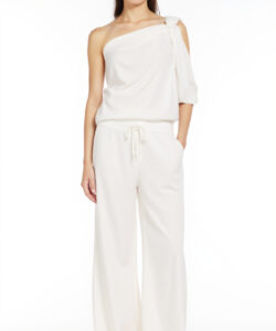 Photograph of a slender woman in white one shoulder top and pants standing against a plain white background