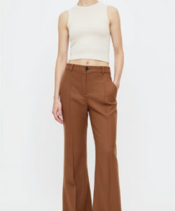 Photograph of a slender woman in white sleeveless top high waisted brown wide leg pants and white shoes standing against a white background